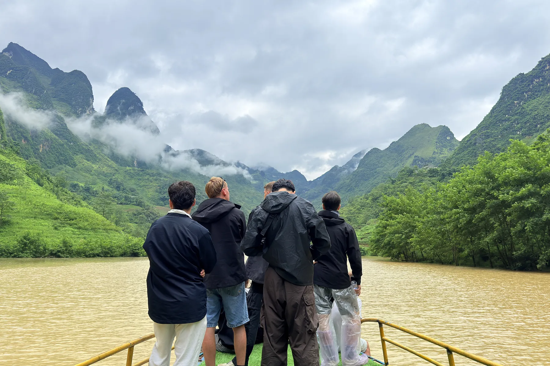 Travellers in raincoats viewing green mountains from a boat after rain
